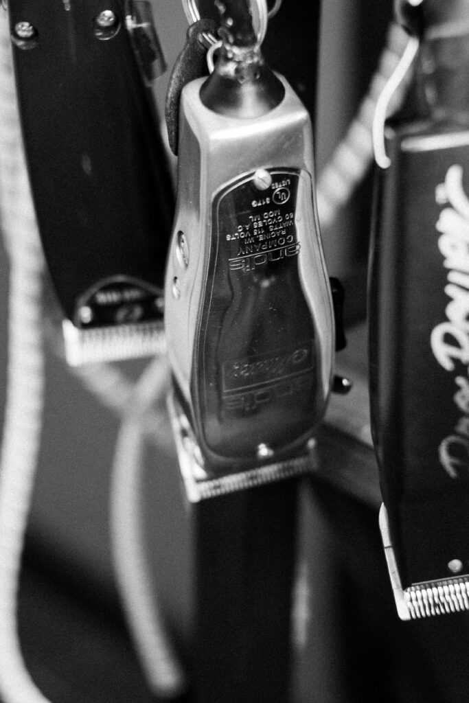 Grayscale image of vintage barber tools including hair clippers on a rack, emphasizing texture and detail.